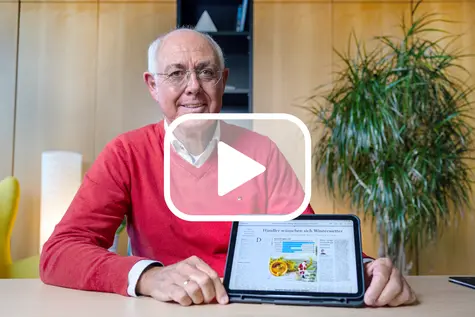 Mann sitzt am Tisch und hält ein Tablet mit der E-Paper-App in die Kamera