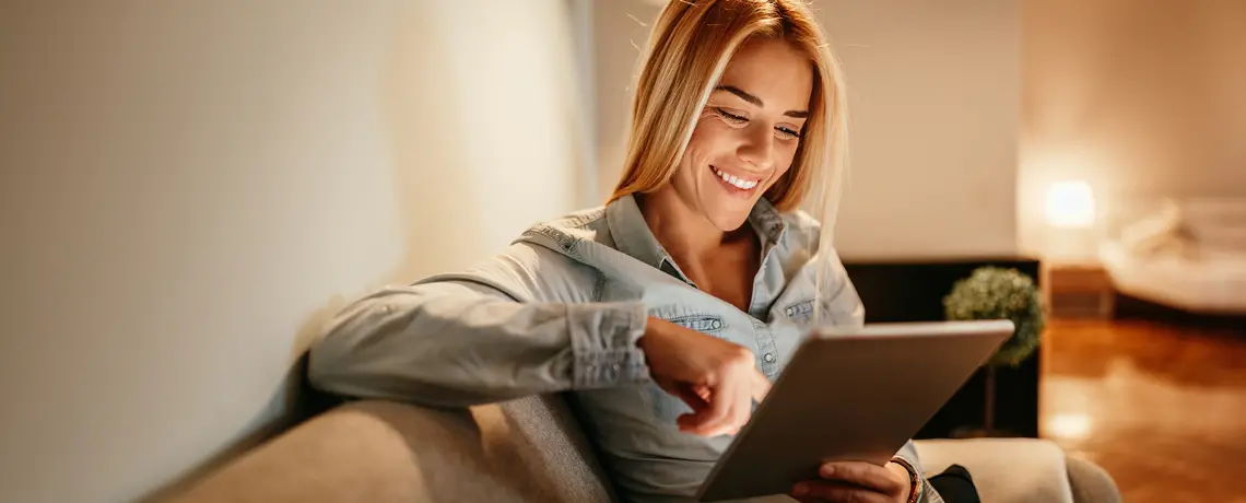 Junge Frau sitzt auf dem Sofa und scrollt auf dem Tablet