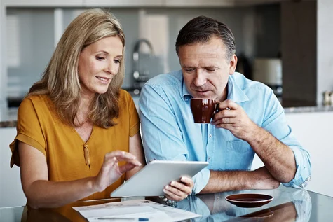 Eine Frau und ein Mann sitzen am Tisch und schauen auf ein Tablet