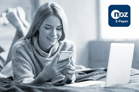 Eine Frau, die im Bett liegt und auf ihr Handy schaut. Neben ihr steht ein Laptop